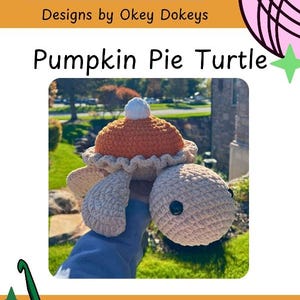 May include: A crochet turtle toy featuring a shell designed to look like a pumpkin pie with a white dollop on top. The turtle has a light beige head and flippers with black button eyes. The text Okey Dokeys Designs by Okey Dokeys Pumpkin Pie Turtle is visible.
