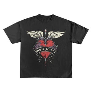 May include: Black t-shirt featuring a distressed graphic. The design includes a red heart pierced by a sword, with wings and roses. The text "BON JOVI" is displayed on a banner below the heart. The shirt has a classic crew neck.