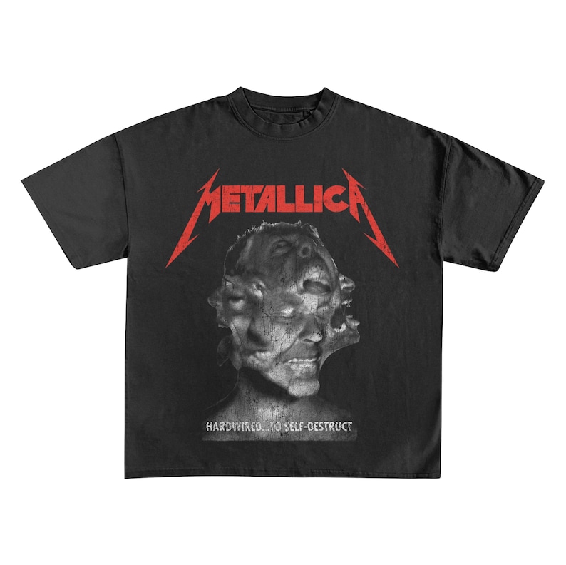 May include: Black t-shirt featuring the band name "Metallica" in red, above a distorted face graphic. The text "HARDWIRED...TO SELF-DESTRUCT" is printed below the graphic. The shirt is a classic crew neck style.