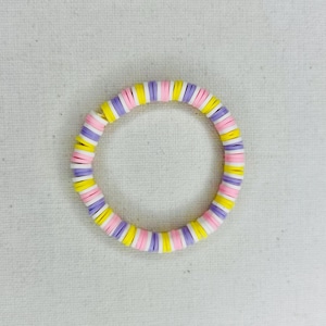 Puede incluir: Un brazalete colorido hecho de cuentas redondas apiladas en rosa, amarillo y morado.