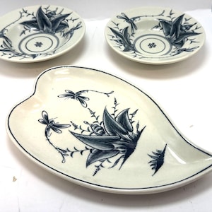 May include: A set of three ceramic dishes with a cream background and a blue floral and dragonfly design. The set includes two small bowls and a leaf-shaped platter, all with a dark blue trim.
