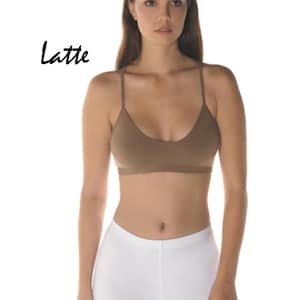 May include: A woman is wearing a brown spaghetti strap crop top and white leggings. The word "Latte" is written in black cursive above her head.