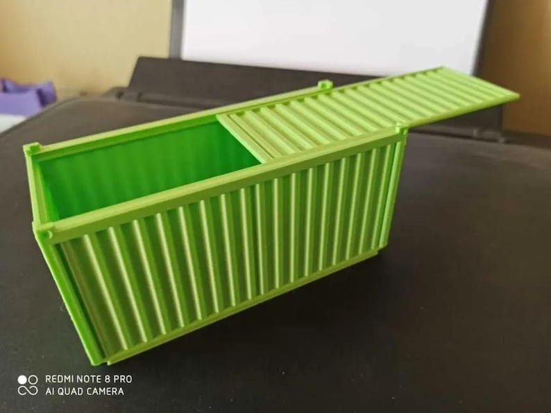 May include: A green plastic toy shipping container with a hinged lid. The container is open and the lid is propped up.