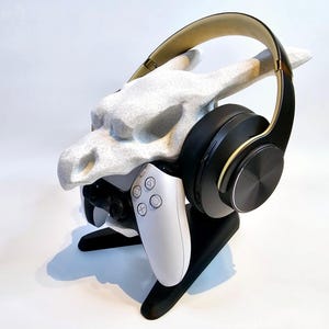 May include: A white dragon-shaped stand with a black and gold headset and a white video game controller.
