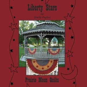 May include: A red, white, and blue quilt pattern with stars and a crescent moon design. The quilt is displayed in a gazebo with a wooden frame and a shingled roof. The text "Liberty Stars" and "Prairie Moon Quilts" is displayed on the image.