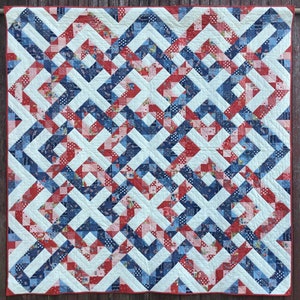 May include: A quilt with a geometric pattern in red, white, and blue. The quilt is made of patchwork squares and triangles.
