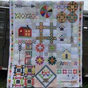 May include: A colorful patchwork quilt with a variety of geometric patterns and designs, including a house, a cross, a basket, and arrows. The quilt is made with a variety of fabrics in shades of red, green, blue, yellow, and white.