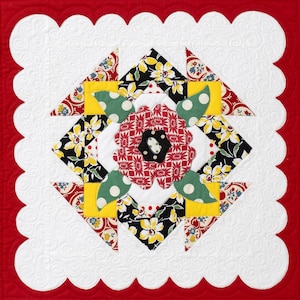 Op de afbeelding: Een wit quiltblok met een rood, wit en groen bloemmotief. Het blok is omgeven door een gegolfde rand.