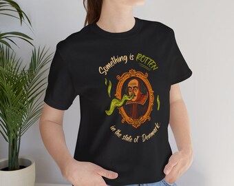 以下が含まれることがあります： 黒いTシャツ。シェイクスピアの肖像画が装飾的なフレームに収められています。「Something is Rotten in the state of Denmark」のテキストが肖像画の上と下に印刷されています。緑色の舌のような形が肖像画から伸びています。