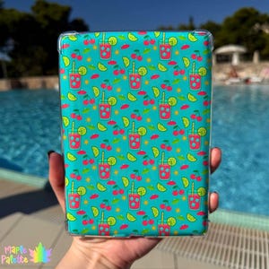 May include: A turquoise tablet case featuring a repeating pattern of red cocktails, cherries, lime slices, and suns. The case is held in a hand, with a pool in the background. The Maple Palette logo is in the bottom left corner.