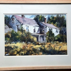 May include: Watercolor painting of a weathered, two-story white house with a red roof, set amidst overgrown foliage. The artwork is framed in a light wood frame, showcasing a rural landscape scene.