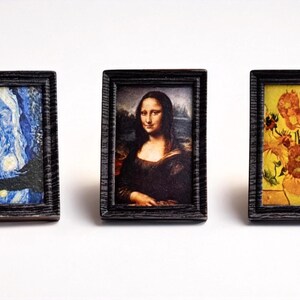 May include: Three miniature framed art prints. The prints feature famous artworks: Van Gogh's "Starry Night", the Mona Lisa, and Van Gogh's "Sunflowers". The frames are dark wood with a textured appearance.