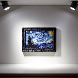 May include: Miniature framed artwork depicting Van Gogh's "Starry Night" painting. The artwork is displayed in a small, white, illuminated display case. The painting features swirling blue and yellow colors, with a dark, textured frame.