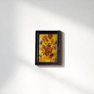 May include: A miniature framed painting of flowers in a vase, reminiscent of Van Gogh's style. The artwork features a yellow vase with orange and yellow flowers, set against a yellow background. The frame is dark brown.