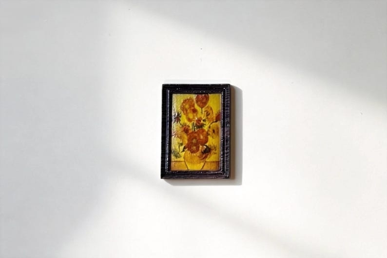 May include: A miniature framed painting of flowers in a vase, reminiscent of Van Gogh's style. The artwork features a yellow vase with orange and yellow flowers, set against a yellow background. The frame is dark brown.