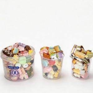 May include: Three clear containers filled with miniature, colorful food-shaped charms. The charms include cakes, cookies, and candies. The largest container has the text "store ware 500" printed on it.