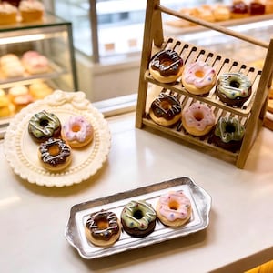 May include: An assortment of miniature donuts with colorful frosting and toppings. The donuts are arranged on a decorative wooden rack, a silver tray, and a white plate. The donuts have chocolate, pink, and green frosting.