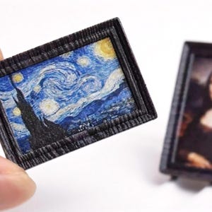 May include: Miniature framed artwork featuring Van Gogh's "Starry Night" painting. The frame is dark with a textured appearance. Another miniature framed artwork of the Mona Lisa is also visible. These are likely dollhouse accessories or decorative items.