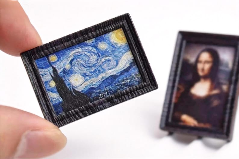 May include: Miniature framed artwork featuring Van Gogh's "Starry Night" painting. The frame is dark with a textured appearance. Another miniature framed artwork of the Mona Lisa is also visible. These are likely dollhouse accessories or decorative items.