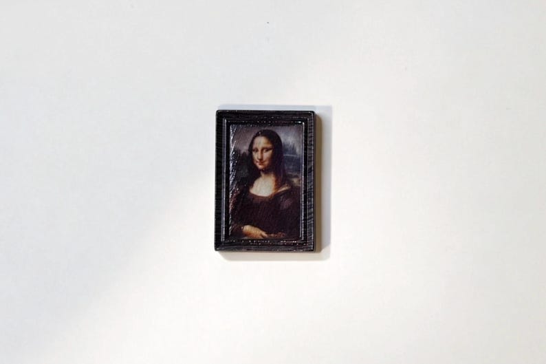 May include: A small, rectangular framed print of the Mona Lisa painting. The frame is dark brown with a textured appearance. The artwork features the iconic portrait of a woman with a subtle smile, rendered in warm, earthy tones.