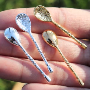 May include: Three miniature spoons with twisted handles. One spoon is silver with a plain bowl, one is silver with a patterned bowl, and one is gold with a plain bowl.