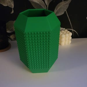 May include: A green hexagonal vase with a textured surface resembling Lego bricks.