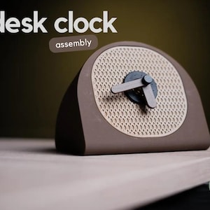 May include: A brown desk clock with a beige face and a honeycomb pattern. The clock has a simple design with black hands and a black centre. The clock is labelled "desk clock assembly".
