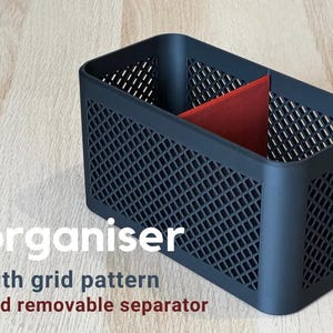 Pode incluir: Organizador de plástico preto com padrão de grade e um separador vermelho removível. O organizador é ideal para guardar itens pequenos como canetas, lápis e outros materiais de escritório.