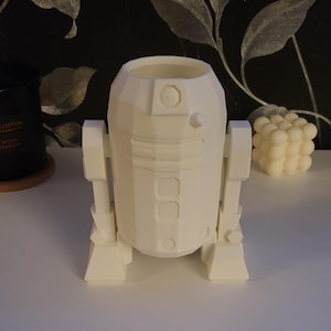 Può includere: Un modello di robot stampato in 3D di colore bianco, che ricorda R2-D2 di Star Wars. Il robot ha un corpo cilindrico con una cupola rotonda sulla parte superiore e due braccia rettangolari.