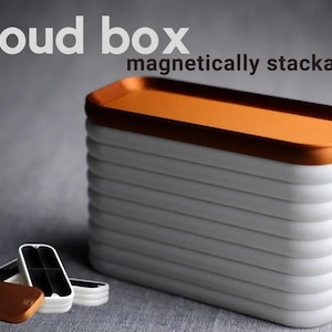 May include: A stackable set of white boxes with a copper top. The boxes are magnetically stackable and have a rounded edge. The text "cloud box magnetically stackable" is printed on the background.