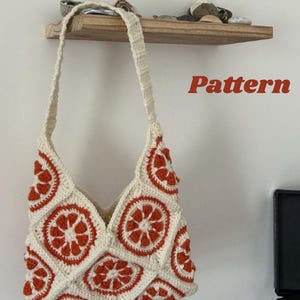 May include: A cream-colored crochet tote bag with orange citrus slice designs. The bag has a long strap and is hanging on a wall. The text "Citrus Breeze Tote" and "Pattern" are visible.