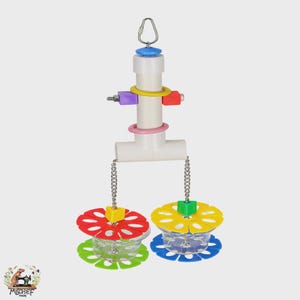 May include: A colorful bird toy with a white PVC pipe structure, featuring a hanging loop, and various colored blocks and rings. Two clear plastic cups with flower-shaped tops in red, green, yellow, and blue hang from chains.