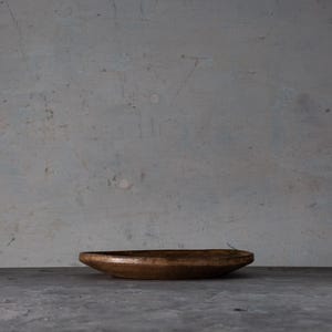 May include: A handcrafted, oval-shaped wooden bowl with a rich, dark brown finish. The bowl sits on a gray surface against a textured, light gray background. The bowl's design suggests it could be used for serving or display.