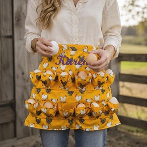 May include: A yellow apron featuring a repeating pattern of white and black chickens, designed with multiple small pockets for holding eggs. The name Karen is embroidered in purple script across the upper section of the fabric.