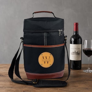 May include: Black insulated wine tote bag with a brown leather base and accents. The bag has a shoulder strap and a handle. A round leather patch with the name "Winslow" is on the front. A bottle of red wine and a wine glass are next to the bag.