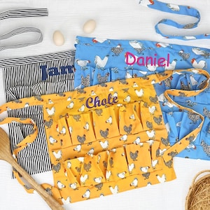 May include: Three waist aprons featuring chicken patterns in black and white stripes, blue, and yellow. The blue apron is embroidered with the name Daniel, the yellow apron with Chole, and the striped apron with Jamie. Each apron includes multiple pockets.