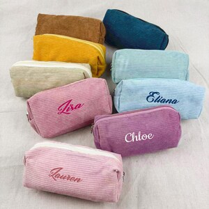 May include: A collection of corduroy pencil cases in various colors, including brown, yellow, teal, light blue, pink, and purple. Some cases have names embroidered on them, such as "Lisa", "Eliana", "Chloe", and "Lauren".