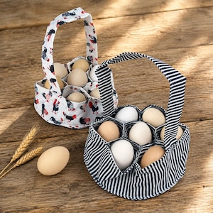 May include: Two fabric egg baskets with handles, one featuring a white background with a rooster pattern and the other with a navy blue and white striped design. Each basket has internal dividers holding multiple light brown and white eggs.