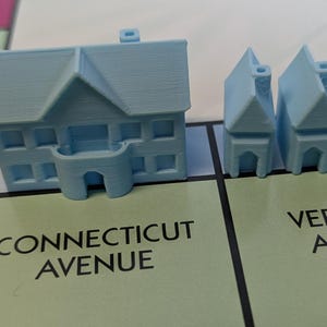 Puede incluir: Una casa de juego de Monopoly azul y cuatro hoteles azules. Las casas est&aacute;n en una casilla verde que dice "Connecticut Avenue" y los hoteles est&aacute;n en una casilla verde que dice "Vermont Avenue".