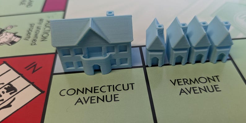 Puede incluir: Una casa de juego de Monopoly azul y cuatro hoteles azules. Las casas est&aacute;n en una casilla verde que dice "Connecticut Avenue" y los hoteles est&aacute;n en una casilla verde que dice "Vermont Avenue".