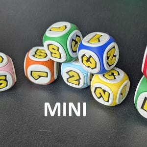 May include: A collection of colorful mini dice featuring white faces with bold yellow numbers. The dice are red, green, blue, yellow, orange, pink, and light blue. The word MINI is printed in white text at the bottom center of the image.