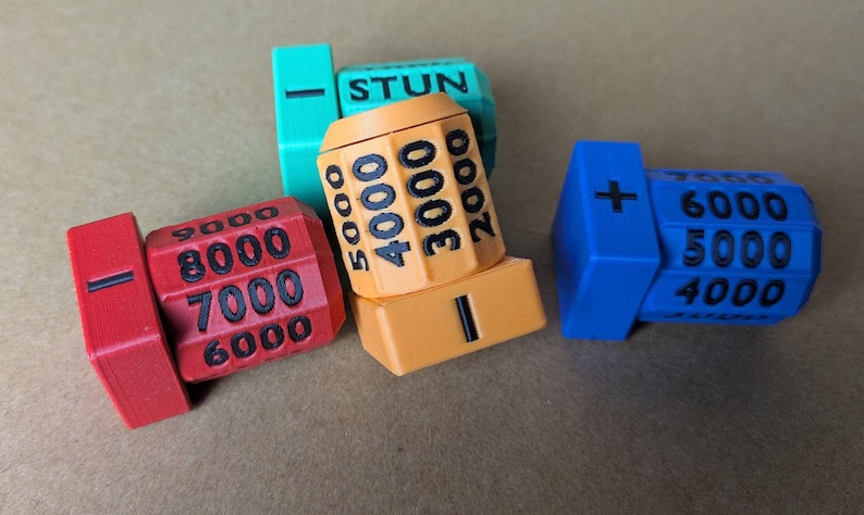 May include: A collection of colourful game dials in red, orange, blue, and green. Each dial features numbers and symbols, with the word "STUN" visible on one. The dials are likely for a board game or electronic device.