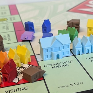 Puede incluir: Un juego de mesa Monopoly con casas y hoteles de varios colores, incluyendo marr&oacute;n, rojo, amarillo, azul y verde. El tablero muestra los nombres de las propiedades "Connecticut Avenue", "Vermont Avenue" y "Visiting".