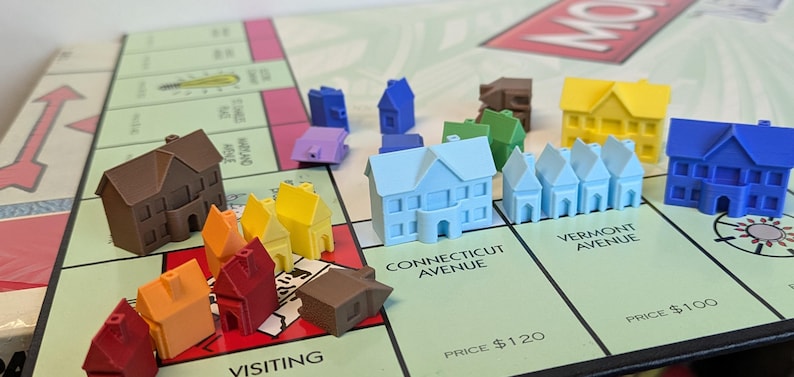 Puede incluir: Un juego de mesa Monopoly con casas y hoteles de varios colores, incluyendo marr&oacute;n, rojo, amarillo, azul y verde. El tablero muestra los nombres de las propiedades "Connecticut Avenue", "Vermont Avenue" y "Visiting".