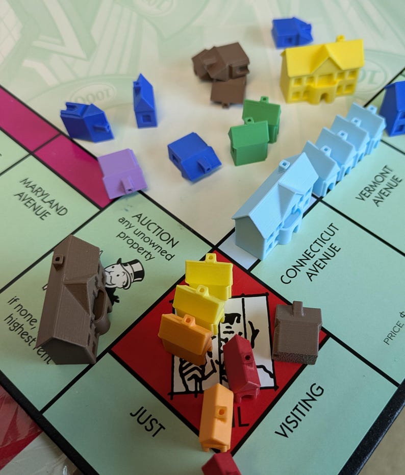 Puede incluir: Primer plano de un tablero de juego de Monopoly con casas y hoteles en varios colores, incluyendo azul, amarillo, rojo y marr&oacute;n. El tablero es verde y tiene las palabras "Maryland Avenue", "Connecticut Avenue", "Vermont Avenue", "Auction", "Just", "Visiting" y "Price 6" impresas en &eacute;l.
