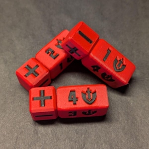 May include: A set of bright red, rectangular gaming dice featuring black embossed markings. The faces display various numbers, plus and minus symbols, and a shield icon with a sword emblem. The dice have a matte, textured finish.