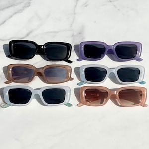 May include: Six pairs of sunglasses in various colors, including black, brown, purple, and blue. The sunglasses have a rectangular frame shape.
