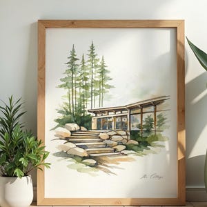 May include: A framed watercolour painting of a modern cottage. The artwork shows a house with large windows, a stone staircase, and trees. The painting is signed "The Cottage" in the bottom right corner. The frame is made of light-colored wood.