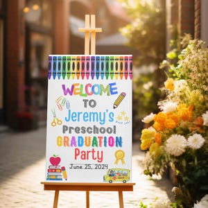 Peut inclure: Une pancarte blanche avec une bordure colorée de crayons, accueillant les invités à la fête de fin d'année de Jeremy à l'école maternelle le 25 juin 2024. La pancarte représente un bus scolaire, une pile de livres, un crayon, des ciseaux et une pomme rouge.