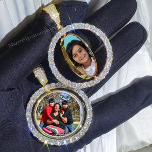 May include: Two gold-tone pendants with a round, clear, diamond-like stone encrusted frame. Each frame holds a photo of a family. The pendant on the left has a photo of a family of three, and the pendant on the right has a photo of a young child.